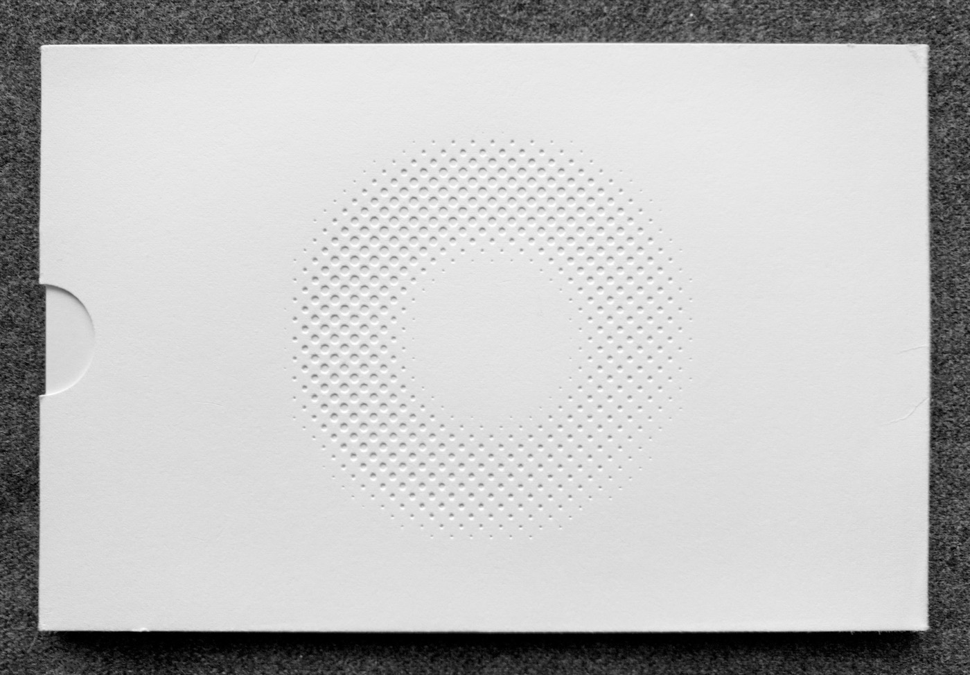 Surface Tension catalogue folder seen from behind, a circular halftone-dot logo blind-embossed at the centre.