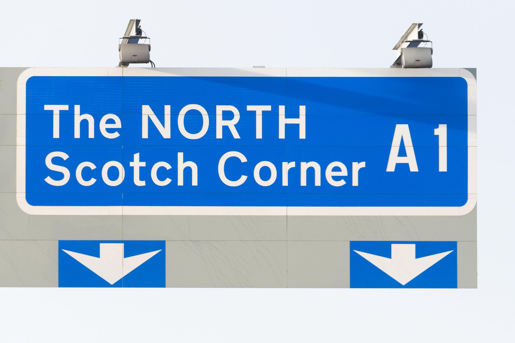A large blue UK motorway sign reading &lsquo;The NORTH, Scotch Corner, A1&rsquo; above two downward lane arrows.